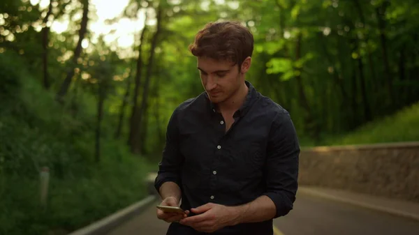 잘생긴 남자가 밖에서 휴대 전화를 꺼내고 있습니다. 공원에서 문자 메시지보내는 남자 — 스톡 사진