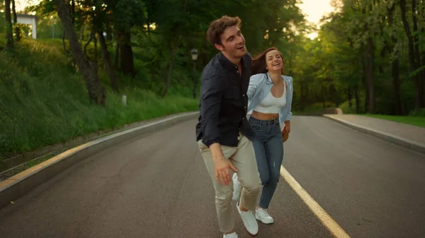 Homem e mulher felizes se divertindo ao ar livre. Casal feliz correndo na estrada no parque — Fotografia de Stock