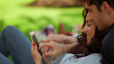 Gülümseyen kız ve yerde yatan adam. Piknikte telefon kullanan neşeli bir çift.