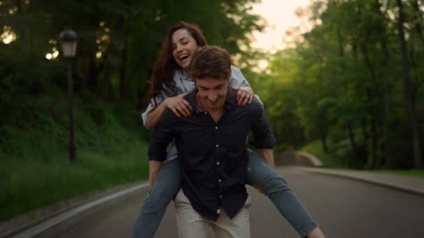 Joven hombre piggyback mujer en romántico fecha en verano parque al atardecer. — Vídeo de stock