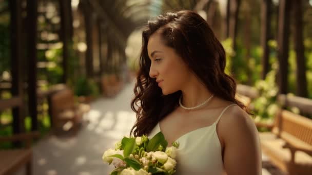 Чудова наречена стоїть під аркою. Красива жінка пахне квітами в саду — стокове відео