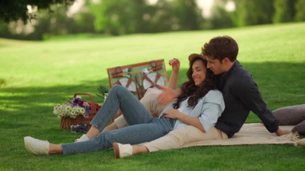 Young man and woman laughing outdoors. Girl and guy sitting on blanket in park — Stock Video