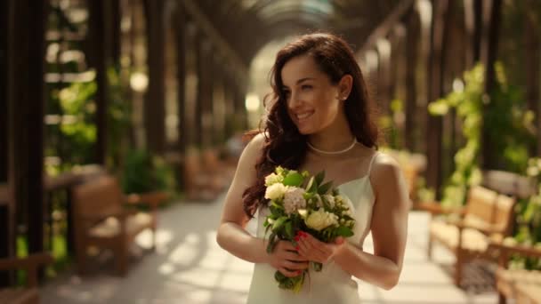 弓の下の花束でポーズを魅力的な花嫁。公園で幸せを感じる女性 — ストック動画