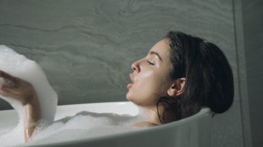 Evde banyo yapan çekici bir kadın. Güzel kız banyoda köpükle eğleniyor..