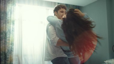 Otel odasında kucaklaşan mutlu çift. Gülümseyen adam ellerinin üzerinde kadının etrafında dönüyor..