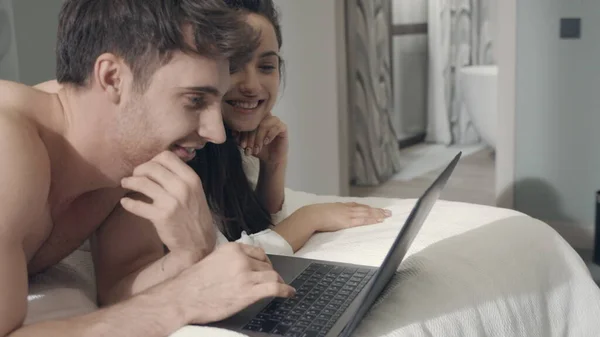 Pareja sorprendida recibiendo portátil de correo electrónico en la cama. Pareja exitosa usando computadora —  Fotos de Stock