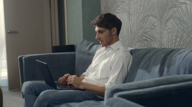 Otel odasında dizüstü bilgisayar kullanan gülümseyen adam. Yakışıklı adam içeride bilgisayarla sohbet ediyor..