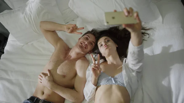 Casal sexy deitado na cama do hotel. lindo homem mulher tomando selfie telefone móvel. — Fotografia de Stock