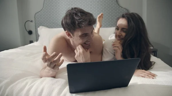 Heyecanlı çift yatakta bilgisayar ekranına bakıyor. İçeride konuşan seksi erkek kadın.. — Stok fotoğraf