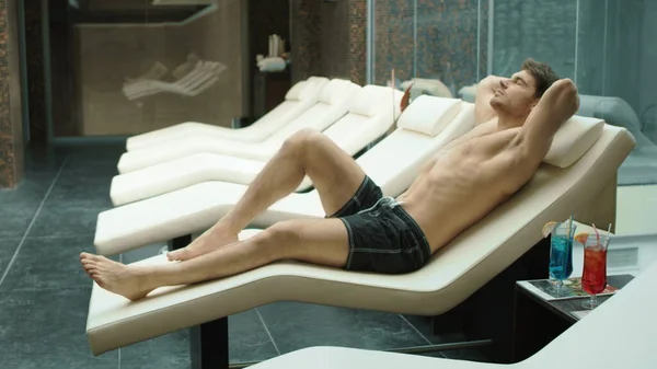 Sportieve man ontspannen in het wellness resort. Sexy kerel liggend op ligstoel in hotel spa. — Stockfoto