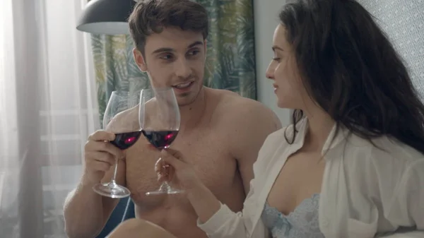 섹시 한 커플이 침대에서 레드 와인을 마시고 있어. 옷 벗은 연인들이 호텔 방에서 이야기하는 모습. — 스톡 사진