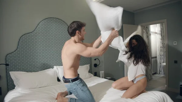 Casal sorrindo um ao outro no quarto de hotel. Casal alegre jogando travesseiros na cama. — Fotografia de Stock