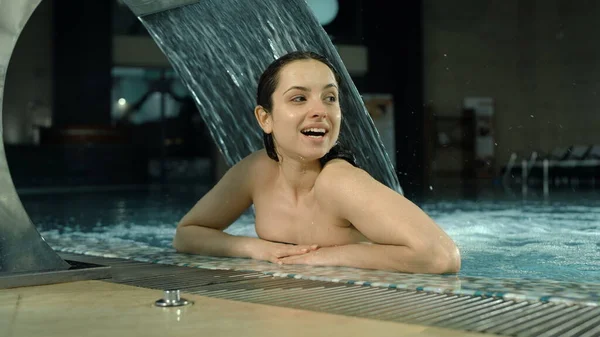 Mujer coqueta sonriendo en la lujosa piscina de spa. Chica alegre agitando la mano desde el jacuzzi. — Foto de Stock