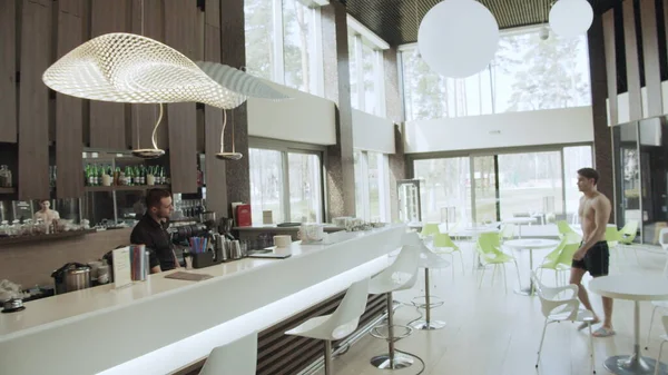 Junger Mann zieht in Bar im Wellness-Resort. Kerl nimmt Flasche Wasser bar counter. — Stockfoto