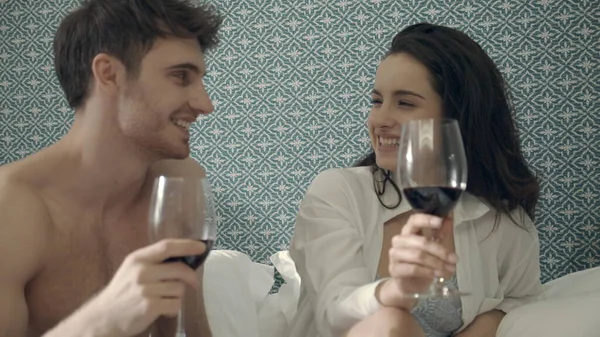 Alegre pareja levantando copas tostadas de vino en la cama. Encantadores amantes de divertirse. — Foto de Stock