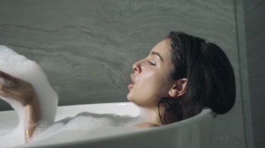 Evde banyo yapan çekici bir kadın. Güzel kız banyoda köpükle eğleniyor..