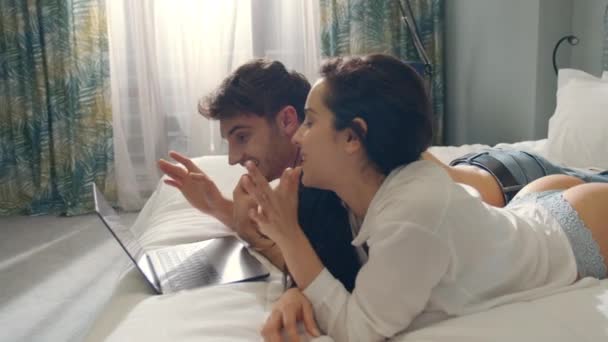 Pareja sonriente que tiene un portátil de videollamadas en la cama. Pareja mirando la pantalla del ordenador. — Vídeos de Stock