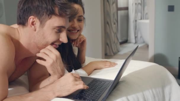 Surprised couple receiving email laptop in bed. Successful couple using computer — Stock Video