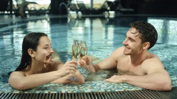 Beautiful couple clinking glasses in spa pool. Man and woman flirting in jacuzzi — Stock Video