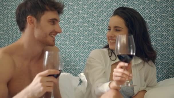 Fröhliches Paar hebt Toastgläser mit Wein im Bett. Charmante Liebhaber, die Spaß haben. — Stockvideo