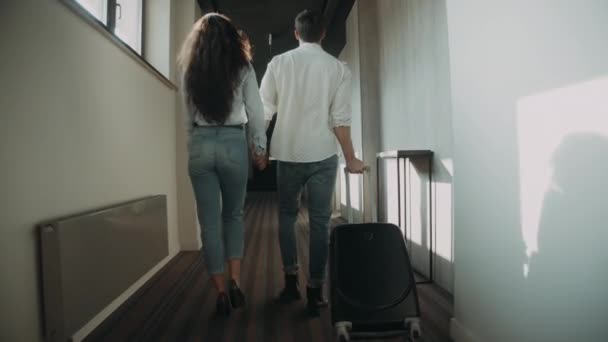 Pasangan manis menarik koper di koridor. Pasangan muda berpegangan tangan di hotel — Stok Video