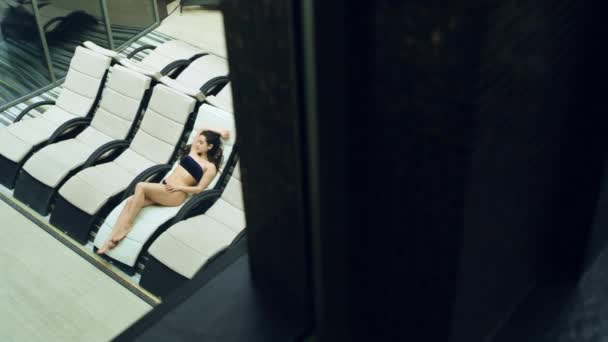 Durch den Fensterblick hübsches Mädchen auf Liegestühlen im Wellnessbereich liegend. Sexy Frau im Wellnessbereich. — Stockvideo