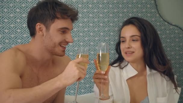 Liefdevol stel flirtend in appartement. Schattig koppel nippen champagne in bed. — Stockvideo