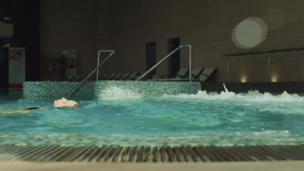 Vacker kvinna simmar på tillbaka i spa pool. Söt tjej som chillar i jacuzzi — Stockvideo