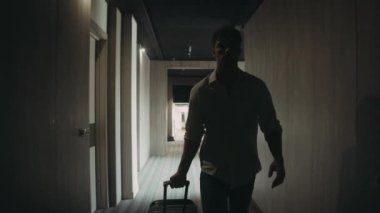 Bagajı olan kendine güvenen bir adam koridor boyunca gidiyor. Adam otel odasını açıyor..