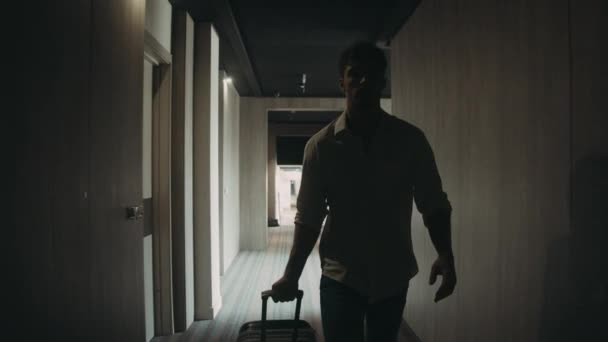 Ένας τύπος με αυτοπεποίθηση και αποσκευές που πηγαίνει κατά μήκος του διαδρόμου. Άνδρας άνοιγμα πόρτα δωμάτιο ξενοδοχείου. — Αρχείο Βίντεο