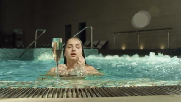 Jolie fille émergeant de l'eau à la piscine spa. Jeune femme sirotant du champagne au spa — Video