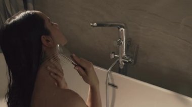 Seksi kadın banyoda duş derelerinin altında oturuyor. Güzel kız küvette dinleniyor..