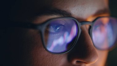 Gözlük, karanlık yerde yansıyan diyagramlara bakıyor. Konsantre tüccarın yüzü, akşam ofisindeki borsa finans verilerini analiz eden bilgisayarla çalışıyor. İnternet 'te sörf yapan kadın uzmanı. 