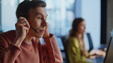 Ajan Hand monitörden kulaklığı alıyor. Çağrı merkezinde çalışan profesyonel teknik asistan bilgisayar görüntüsü. Genç yardım hattı yöneticileri, danışman müşteriyle sohbet ediyorlar. Müşteri desteği işi