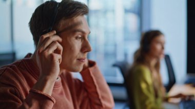 Operatör eli kulaklıkları bilgisayardan alıyor. Genç adam ofisteki çağrı merkezinde danışmanlık yapıyor. Pozitif destek ajanı kulaklıkla konuşuyor. Müşteri hizmetleri yardım hattı kavramı 