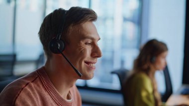 Çağrı merkezinde yakın çekim teknik asistanı konuşuyor. Odaklanmış operatör, müşteri dinleme isteği çevrimiçi çözüldü. Gülümseyen destek ajanı kulaklıkla müşterilere danışmanlık yapıyor. Yardım masası kariyer konsepti