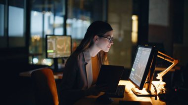 Gerçek zamanlı hisse senetleri ve döviz borsaları ile gece vardiyasında çalışan bir finans analisti. Memnun iş kadını elinde taşınabilir bilgisayarla yatırım bankasında geç saatlere kadar çalışıyor.