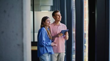 Ekip profesyonelleri uzun pencerelerin yakınında fikir alışverişinde bulunuyorlar. Hırslı iş arkadaşları iş yerinde başarı vizyonunu tartışıyorlar. Tablet aygıtını yöneten çalışma arkadaşları