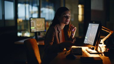 Ofiste geç saatlere kadar çalışan çok çalışan finansör görünümlü monitör. Gözlüklü bir gece kadını bilgisayar şirketine bakıyor. Koyu iş yerinde profesyonel para birimi büyümesi 