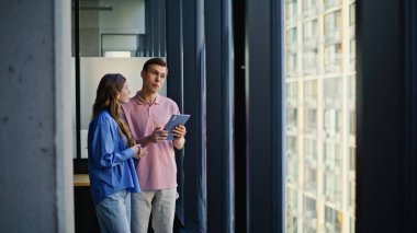 Şirket çalışanları sunumu gözden geçiriyorlar. İş yerinde birlikte tablet aygıt kullanarak iş ilerlemesi öngörüyorlar. Odaklanmış ekip fikir alışverişinde bulunuyor. Pencerenin yakınındaki yol haritasını hazırlıyor.