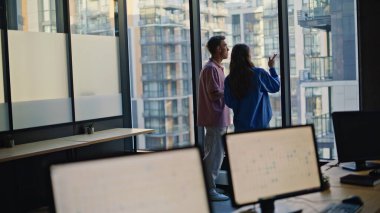 Binadaki cam duvarda duran girişimci hedefleri değerlendiren takım profesyonelleri. Hırslı iş arkadaşları gelecekteki başarılarını sekme cihazıyla tartışıyor. Dijital tablet tutan erkek yönetici yönetim stratejisi