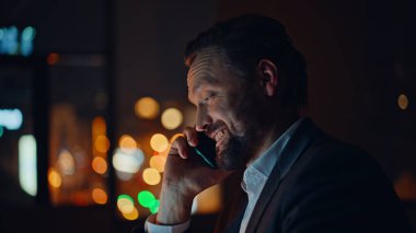 Gece işadamı ofis portresi için cep telefonunu arıyor. Pozitif sakallı adam, akşam iş yerinde cep telefonuyla konuşuyor. Akıllı telefondan konuşan neşeli işçi. 