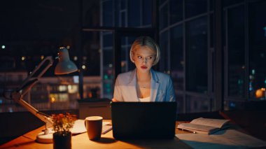 Yaratıcı yönetici video çağrısı proje fikrini karanlık ofis kapanışında açıklıyor. Geceleri dizüstü bilgisayarla konuşan gülümseyen bir kadın. Pozitif sarışının uzak kabinede online iş görüşmesi var.