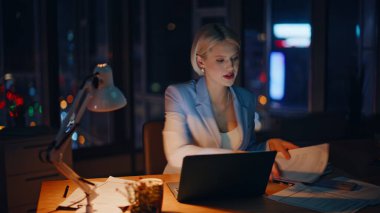 Çalışkan sekreter, karanlık apartman işyerindeki belgeleri inceliyor. Gülümseyen meşgul kadın profesyonel görünümlü dizüstü bilgisayar gece ofisinde kağıtları kontrol ediyor. Fazla mesai yöneticisi son teslim tarihini düşünüyor. 