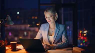 Dizüstü bilgisayarı gece işyerine yakın çekim. Karanlık ofiste ışık altında çalışan gülümseyen bir iş kadını. Gece geç saatlerde online proje geliştiren serbest yazardan esinlendim. Fazla mesai kavramı 