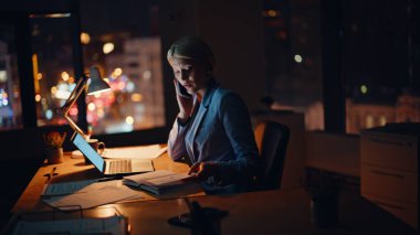 Profesyonel danışman, akşam şirketinin çalışma alanından müşteriyi arıyor. Meşgul kadın yönetici cep telefonuyla konuşuyor. Gece ofisinde dizüstü çalışıyor. Gülümseyen iş kadını cep telefonu konuşmalarıyla projeyi tartışıyor