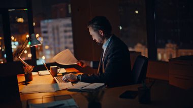 Ofis uzmanı geç saatlere kadar karanlık çalışma alanında çalışıyor. Kontrat belgelerini kontrol etmek için fazla mesai yapan işine odaklanmış bir iş adamı. Ciddi bir yönetici gece vakti kahve yudumlarken dizüstü bilgisayar kullanıyor.