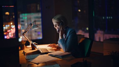 Pozitif yönetici cep telefonunu arıyor iş başarısını tartışıyor gece iş yerinde dizüstü bilgisayarı arıyor. Mesai saatlerinde cep telefonuyla konuşan mutlu bir iş kadını. Gülümseyen kadın rapor veriyor.