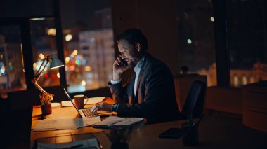 Akşam şirketinin çalışma alanında profesyonel çalışan akıllı telefon görüşmesi. Meşgul bir yönetici, cep telefonunda müşteriyle konuşuyor. Gece ofisinde dizüstü çalışıyor. Gülümseyen işadamı cep telefonuyla projeyi tartışıyor