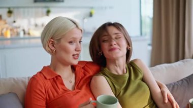 TV 'de rahat bir kanepede film izleyen kız arkadaşlara sarılmak. İki kadın izleyici evde televizyonla vakit geçiriyor. Aşırı neşeli lgbt çifti yumuşak koltukta eğlenceli eğlence programının keyfini çıkarın.